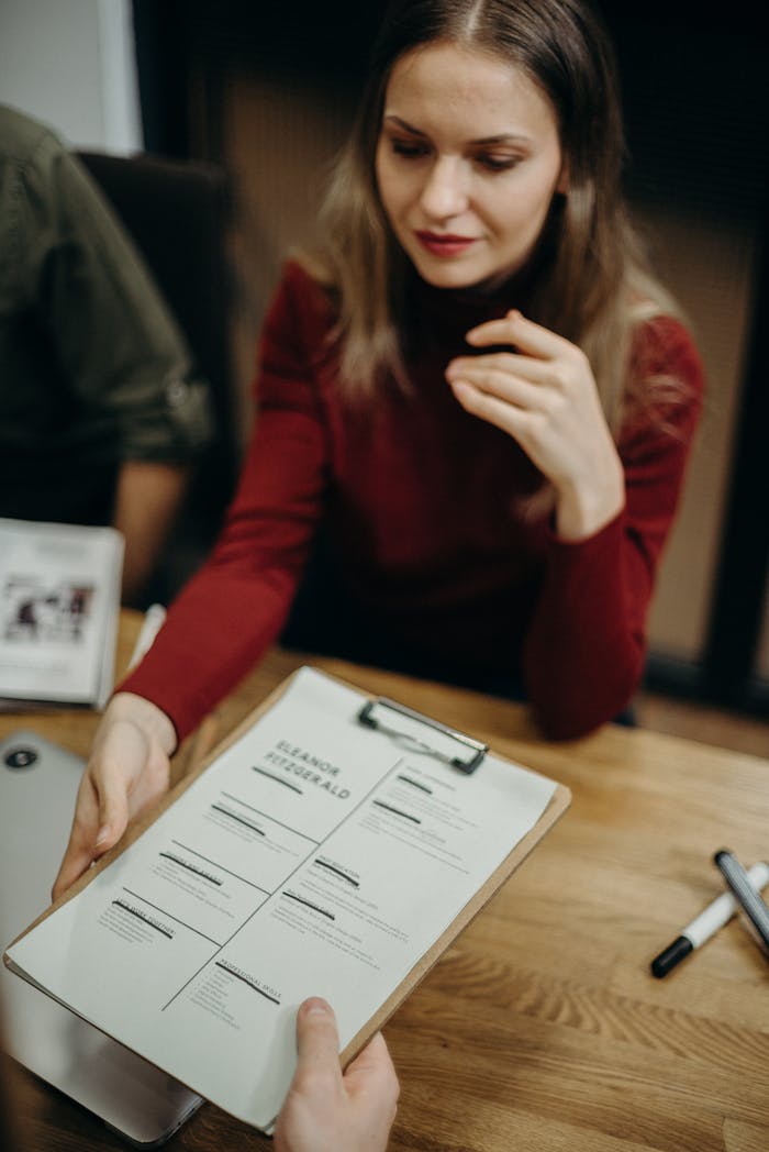 creative-02 Woman sitting at a desk holding a clipboard and reviewing a resume during a job interview.